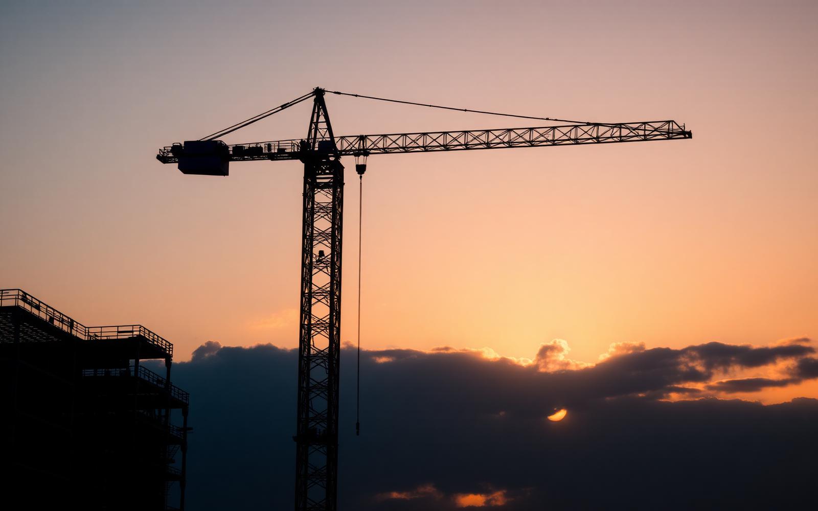Tower crane silhouetted against a dusk sky over a structural steel skeleton