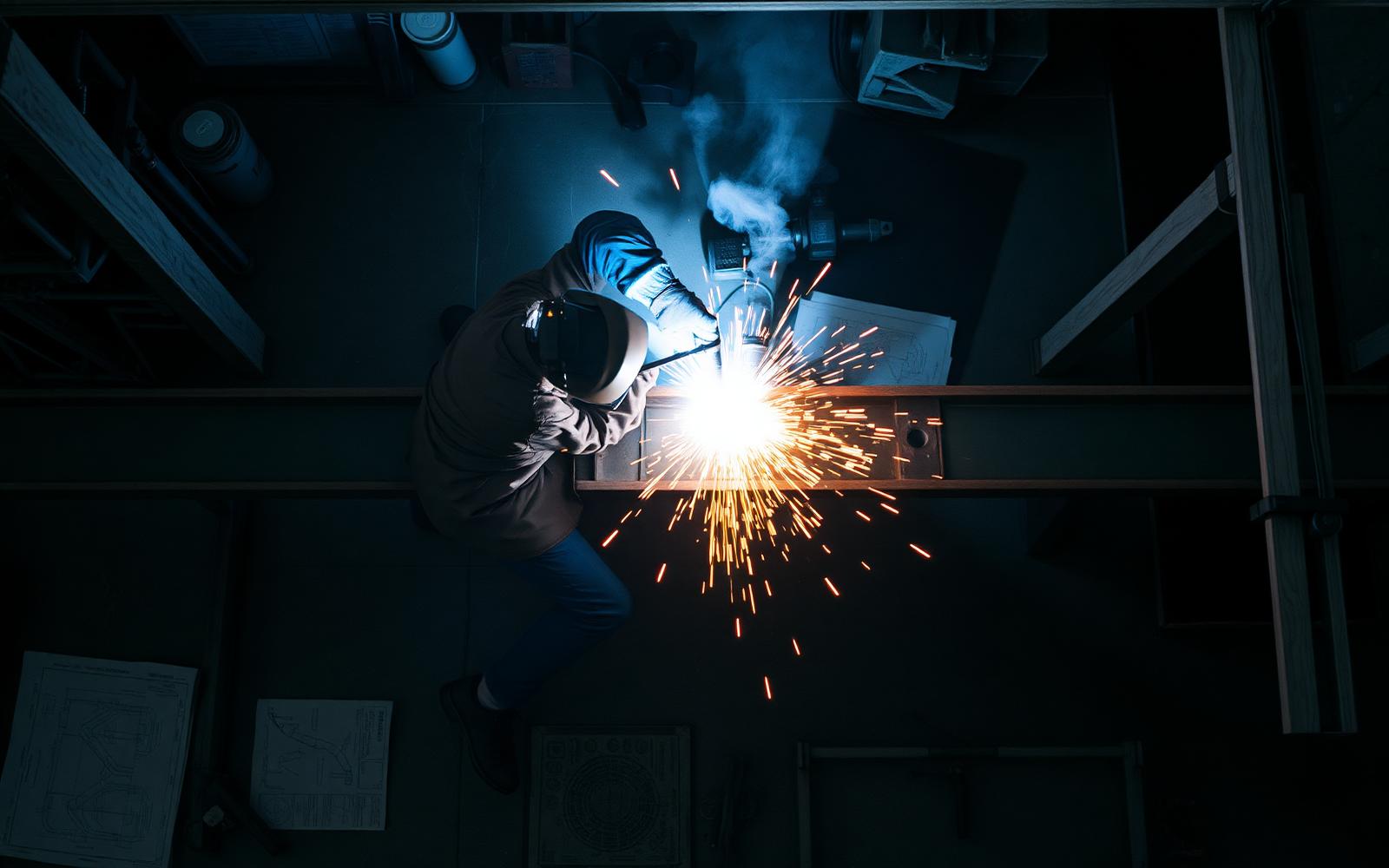 Overhead view of welder striking arc on a structural I-beam with cascading sparks