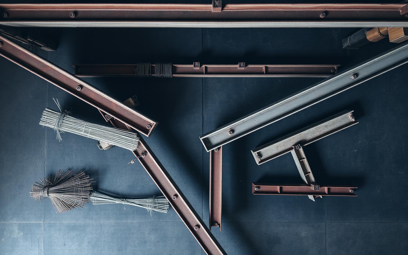 Structural steel beams laid out on the shop floor under overhead crane rails